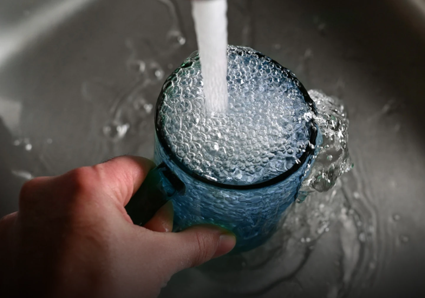 Hand holding glass under running faucet.